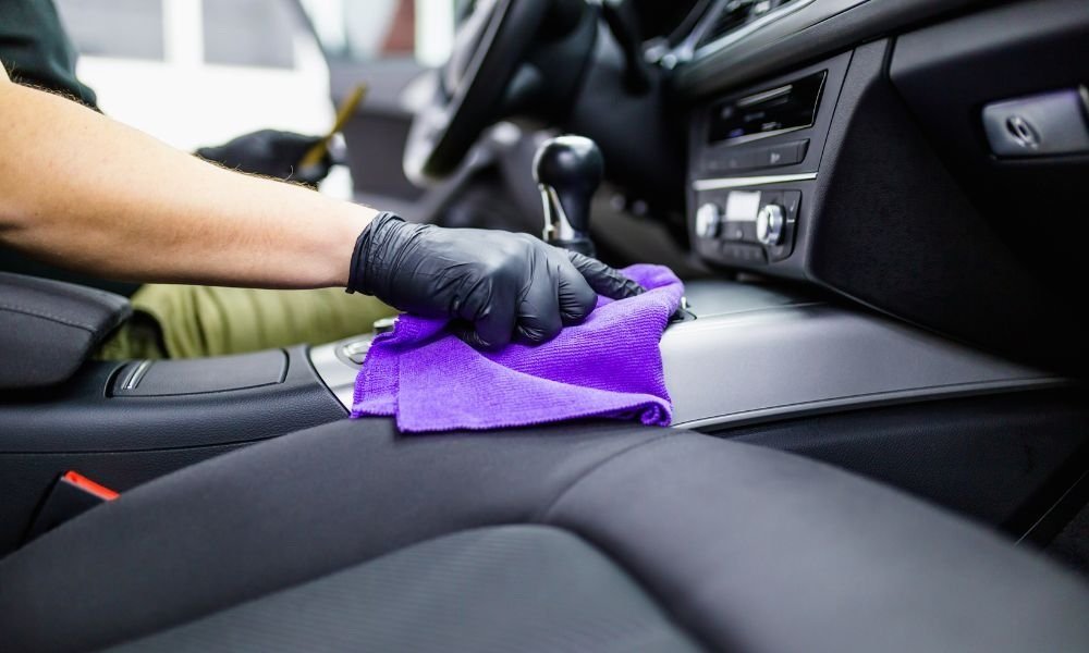 Person wearing gloves cleaning the interior of a car with a purple microfiber cloth, emphasizing the importance of vehicle detailing.