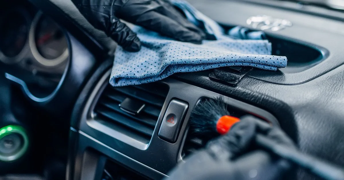 Person wearing gloves cleaning a car interior with a microfiber cloth and detailing brush, emphasizing proper car detailing techniques for maintaining vehicle cleanliness and value.