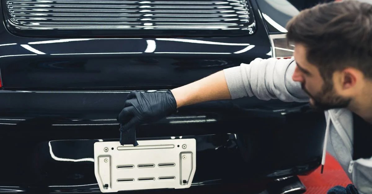 Man applying ceramic coating to the rear of a black car, emphasizing vehicle protection and shine enhancement.
