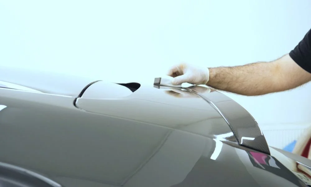 Person applying paint protection film on the rear of a car, emphasizing vehicle maintenance and sun damage prevention.