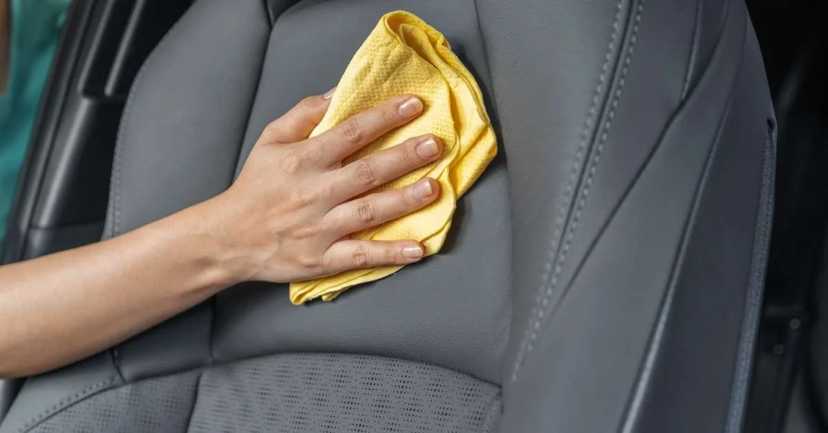Person cleaning leather car seat with a yellow microfiber cloth, highlighting maintenance for leather interiors.