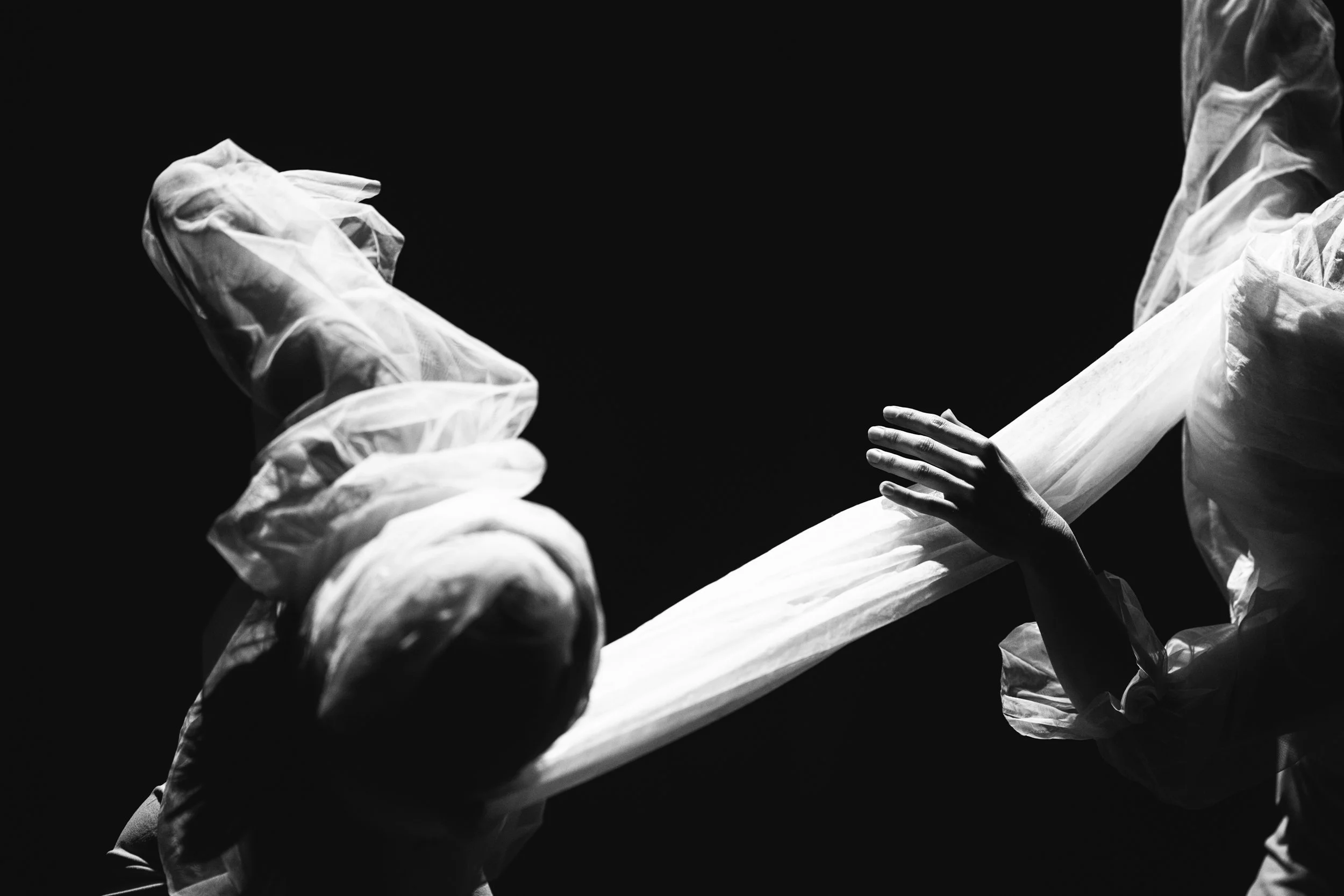 Black and white photo of healthcare workers in protective gear handling a long tube or fabric against a dark background.