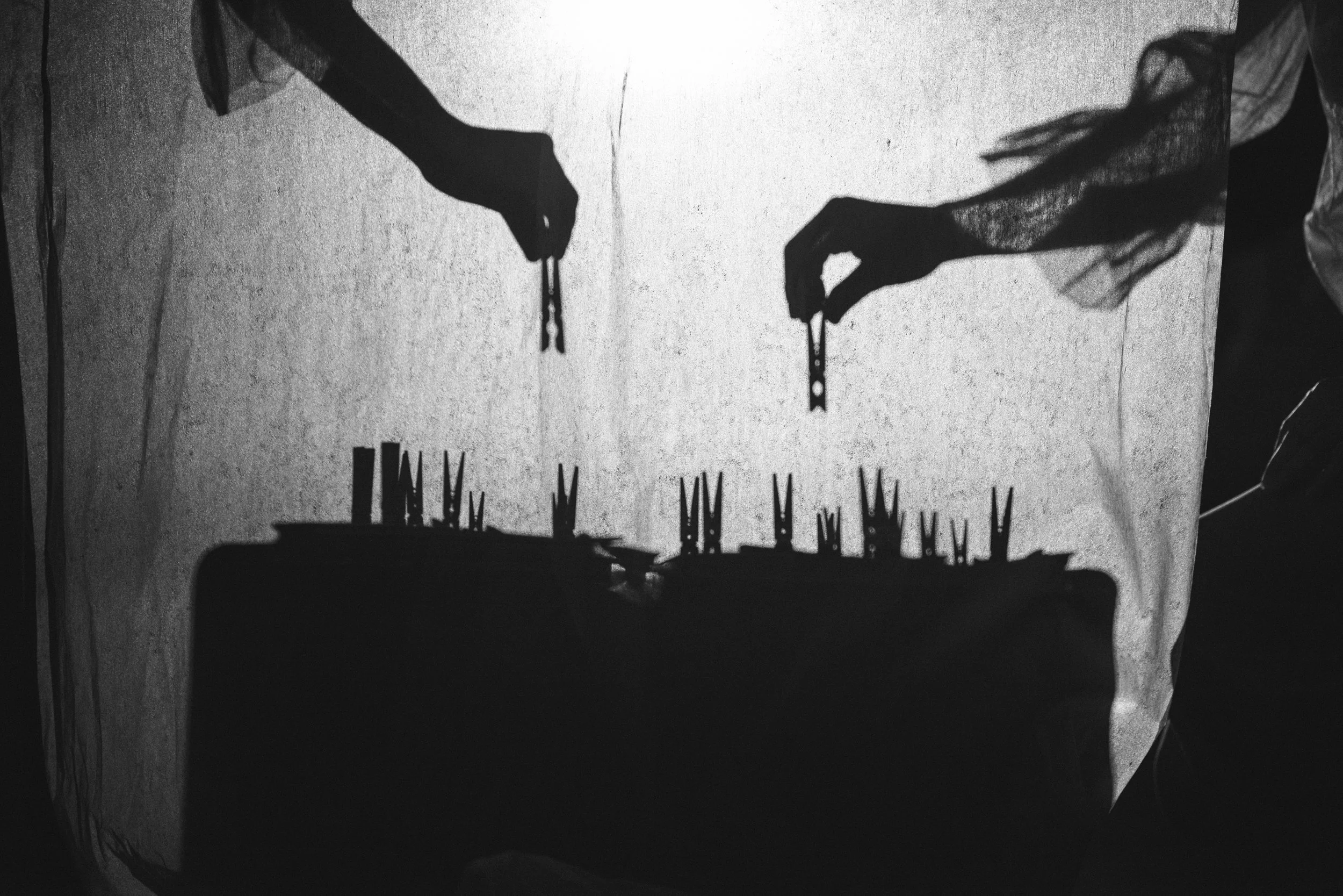 The shadow of two hands reaching towards each other with a small object between their fingers, casting a shadow on a wall with some writing.