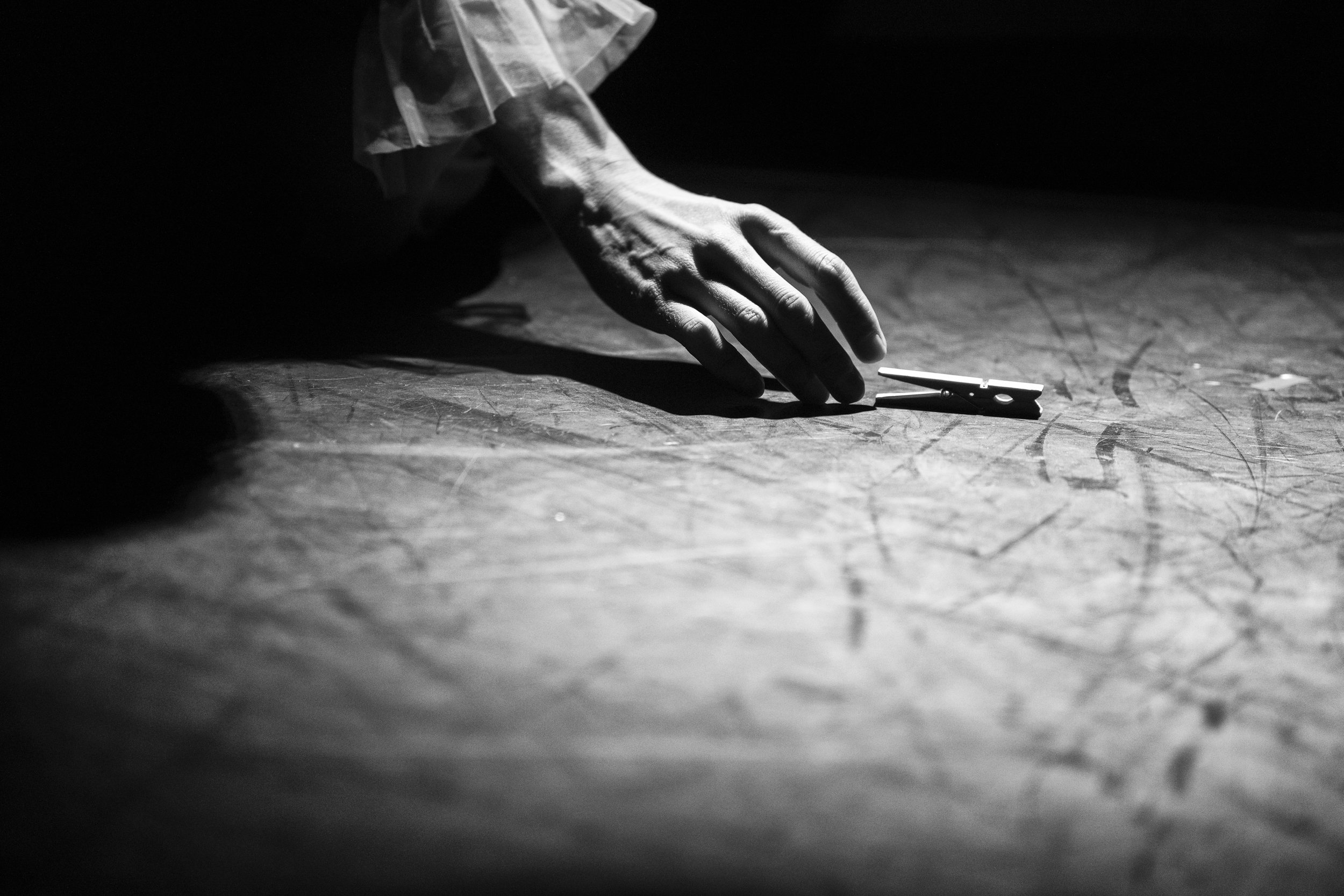 A person's hand reaching for a clothespin on a wooden surface in a dimly lit setting.