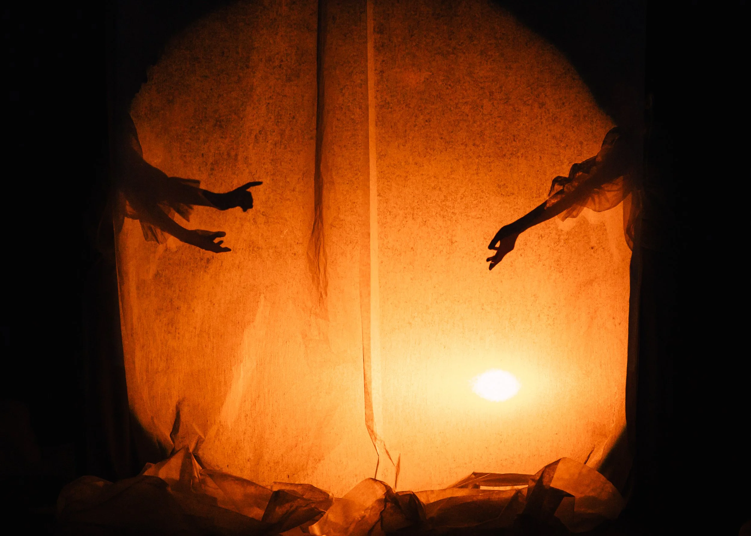Two people release sky lanterns during sunset, with dark silhouettes against an orange sky.