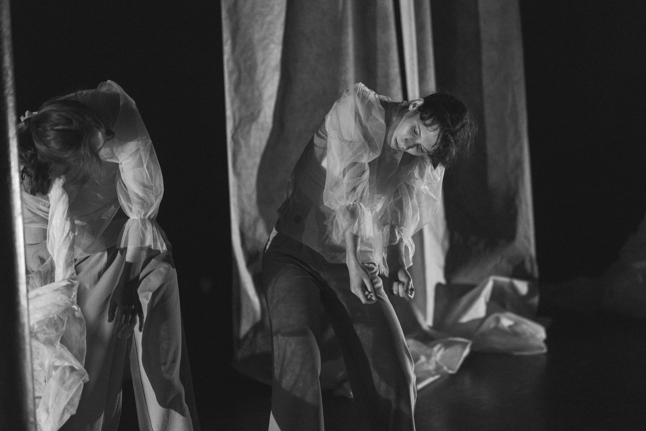 Two young men in protective suits or medical gowns are looking and leaning forward, possibly in a laboratory or medical setting. The image is in black and white.