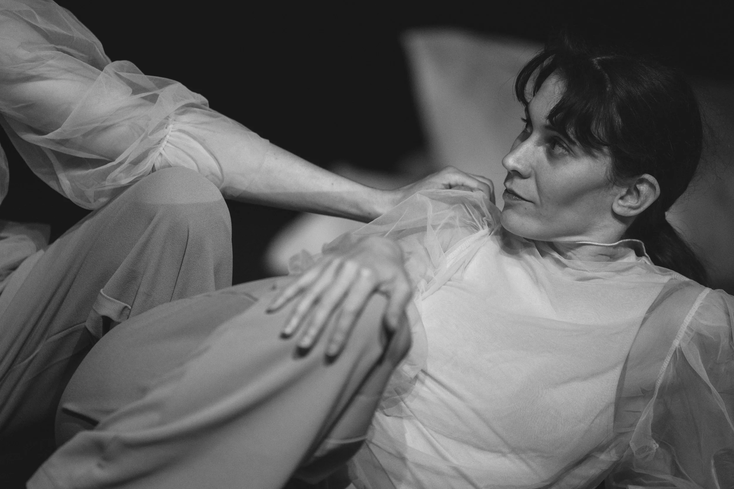 A woman lying down and looking at a person in front of her, with their hand resting on her shoulder. The image is in black and white.