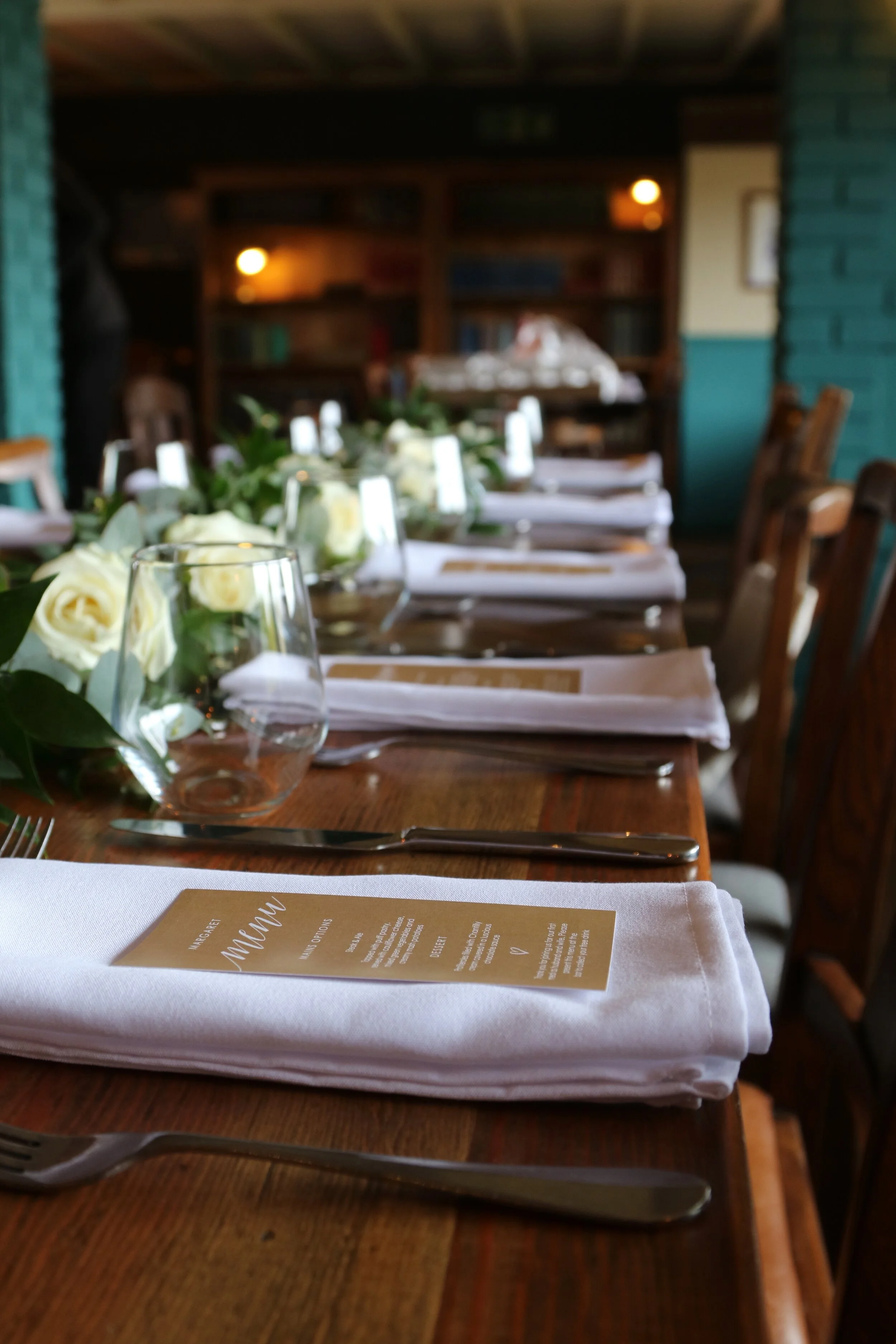 Individual place settings with white ink, wreaths of foliage running along trestle tables.