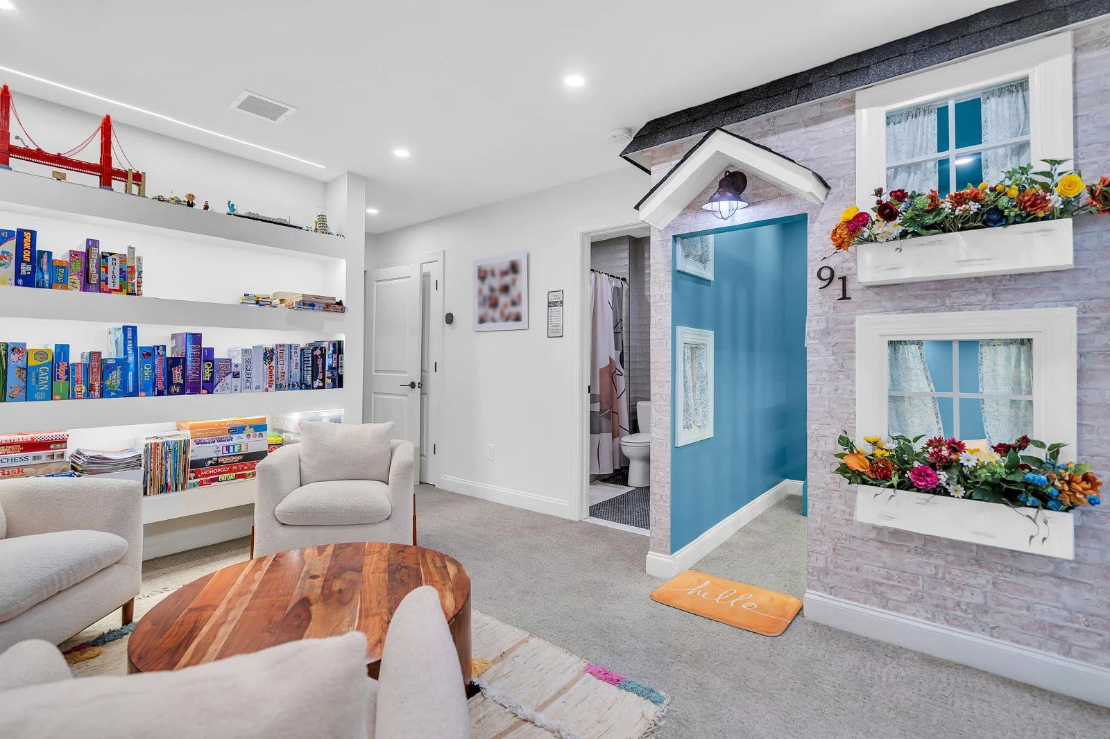 Attic renovation featuring a bespoke custom kids' playhouse with faux brick and a shingled roof, alongside board game area with three ivory bouclé chairs and a wood table.