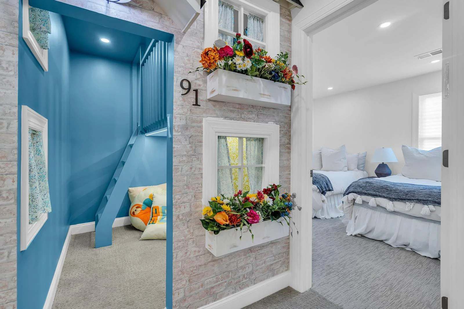 Custom kids' playhouse interior with a teal colorwashed loft layout and ladder, showing unique decorative wallpaper accents and an architectural view into the adjacent guest room.