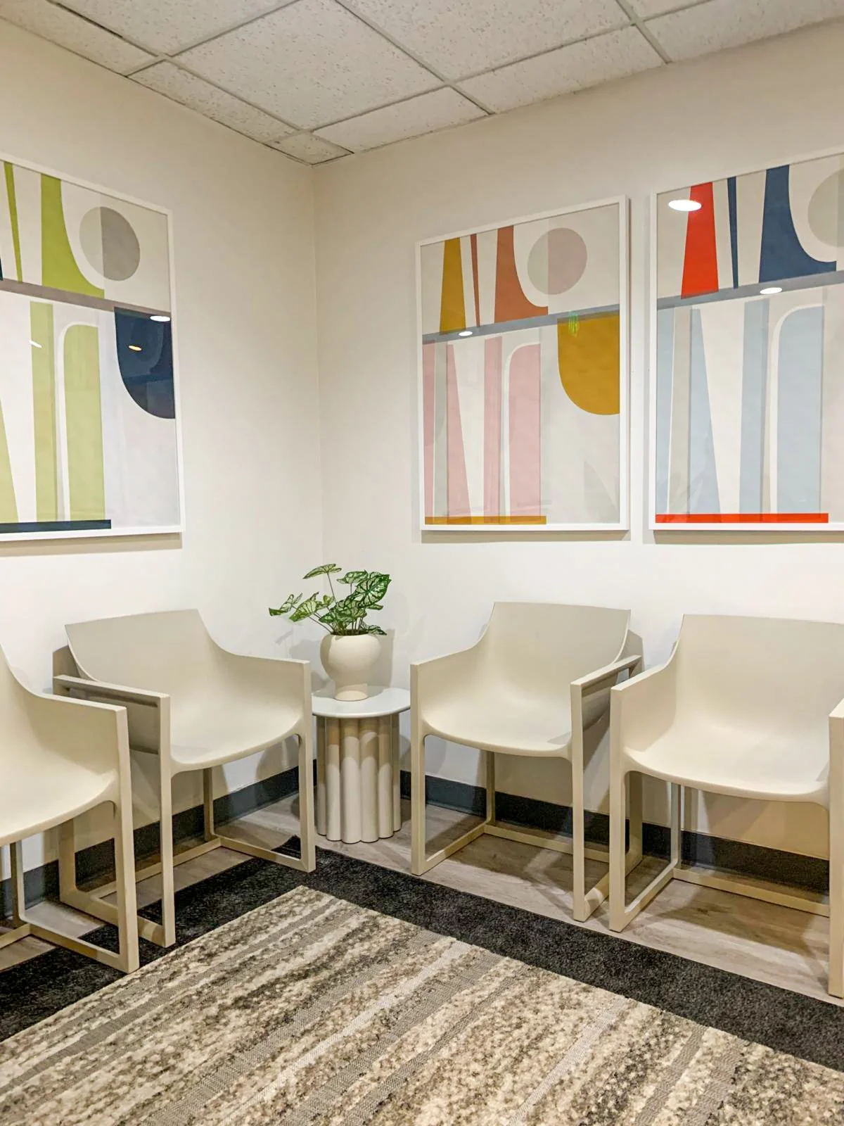 Sleek Beverly Hills medical waiting room featuring molded resin chairs, soothing geometric art, a sculptural side table, faux plants, and a modern high-traffic rug.