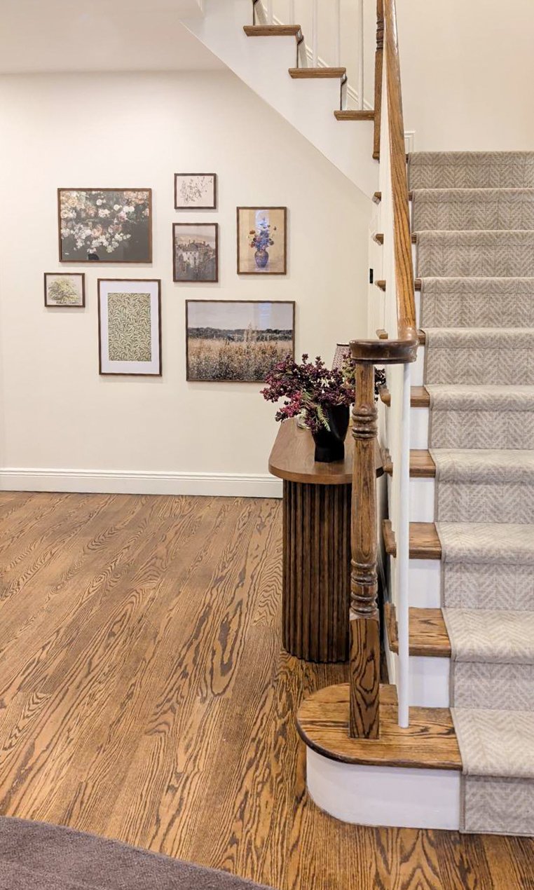 New Jersey home entryway featuring a staircase with a custom runner, a styled reeded wood console table, a curated gallery wall, and an organic chocolate rug to ground the area.