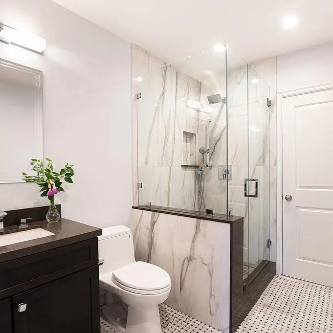 Los Angeles powder room with black, cream, and gray tones, featuring a dramatic veined tile shower, frameless glass pony wall, marble mosaic floor, chrome fixtures, and a dark moody vanity.