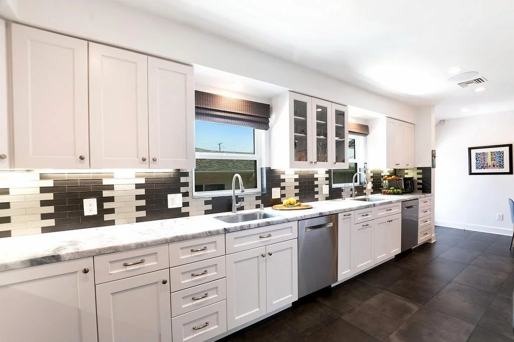 Los Angeles galley kitchen with white cabinetry, white and gray quartzite countertops, decorative glass subway tile backsplash, faux concrete tile floors, and stainless steel appliances.