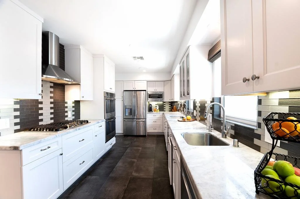 Los Angeles galley kitchen with white cabinetry, white and gray quartzite countertops, decorative glass subway tile backsplash, faux concrete tile floors, and stainless steel appliances.