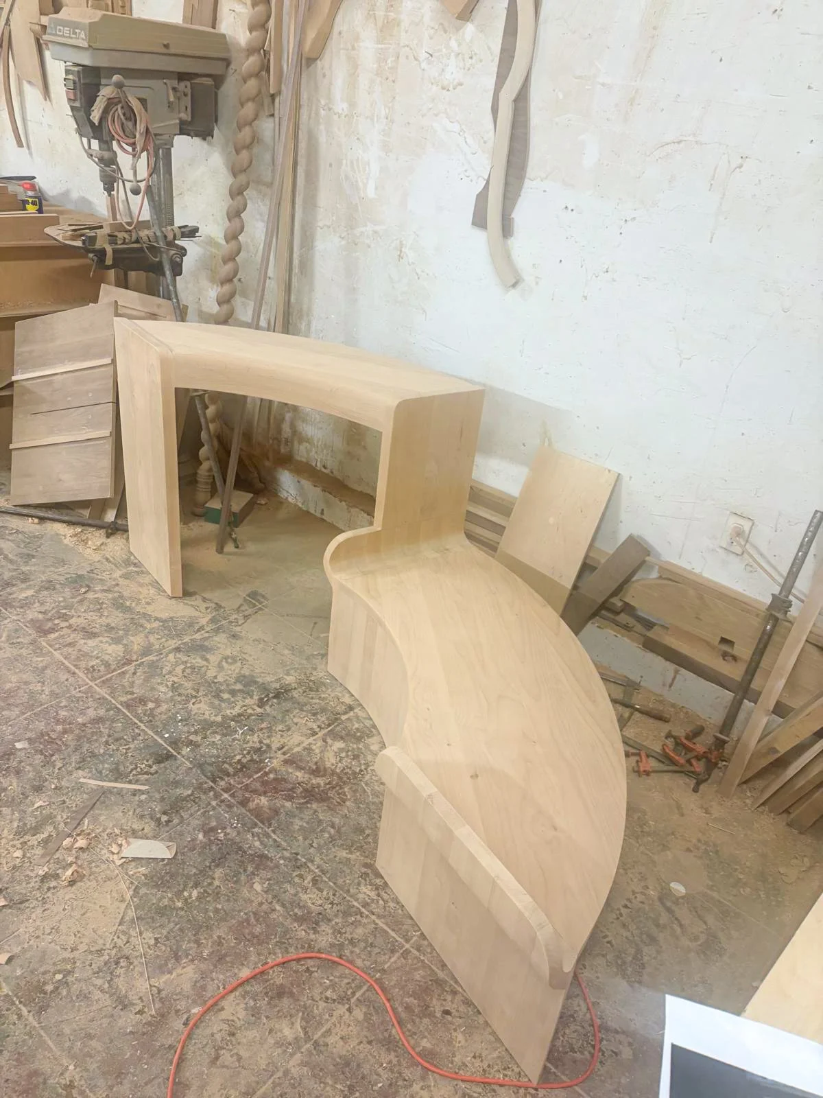 Mid-construction view of the custom curved alder wood console bench frame designed for a specific curved staircase niche, showcasing the raw woodwork before finish application.