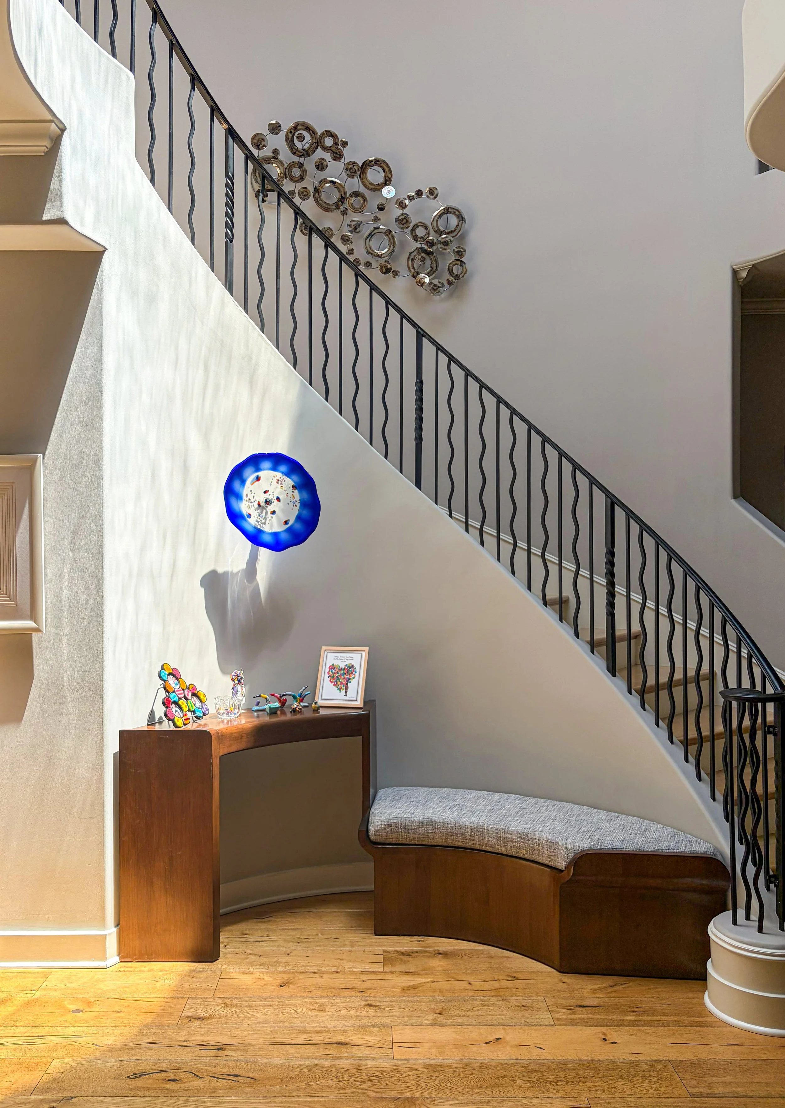 Custom curved alder wood console bench with a performance fabric cushion nestled in a staircase niche, styled with client art and decor.