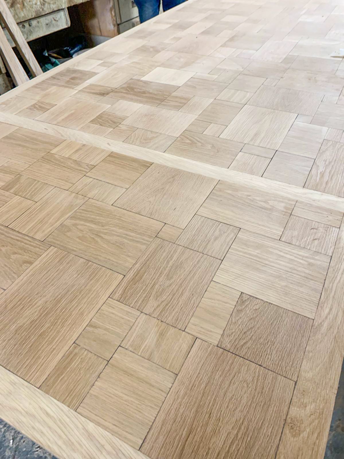 Close-up of a custom white oak parquet dining table mid-construction, highlighting the border detail and the perfectly flush-fit extension leaf.