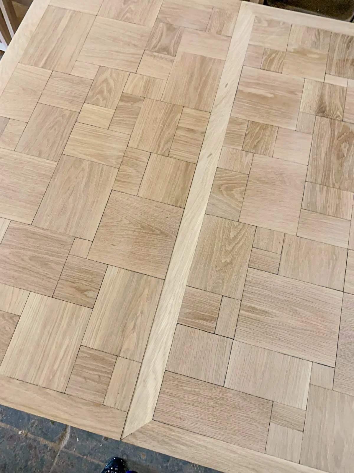 Close-up of a custom white oak parquet dining table mid-construction, highlighting the border detail and the perfectly flush-fit extension leaf.