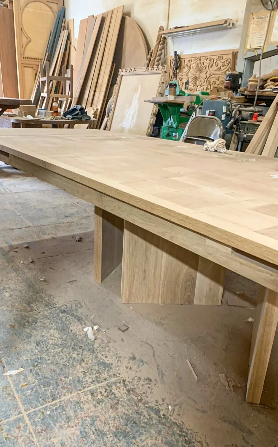 Custom white oak dining table with a parquet top mid-construction. Features self-storing leaf extension pockets and a dynamic, multi-directional three-leg base for visual depth.