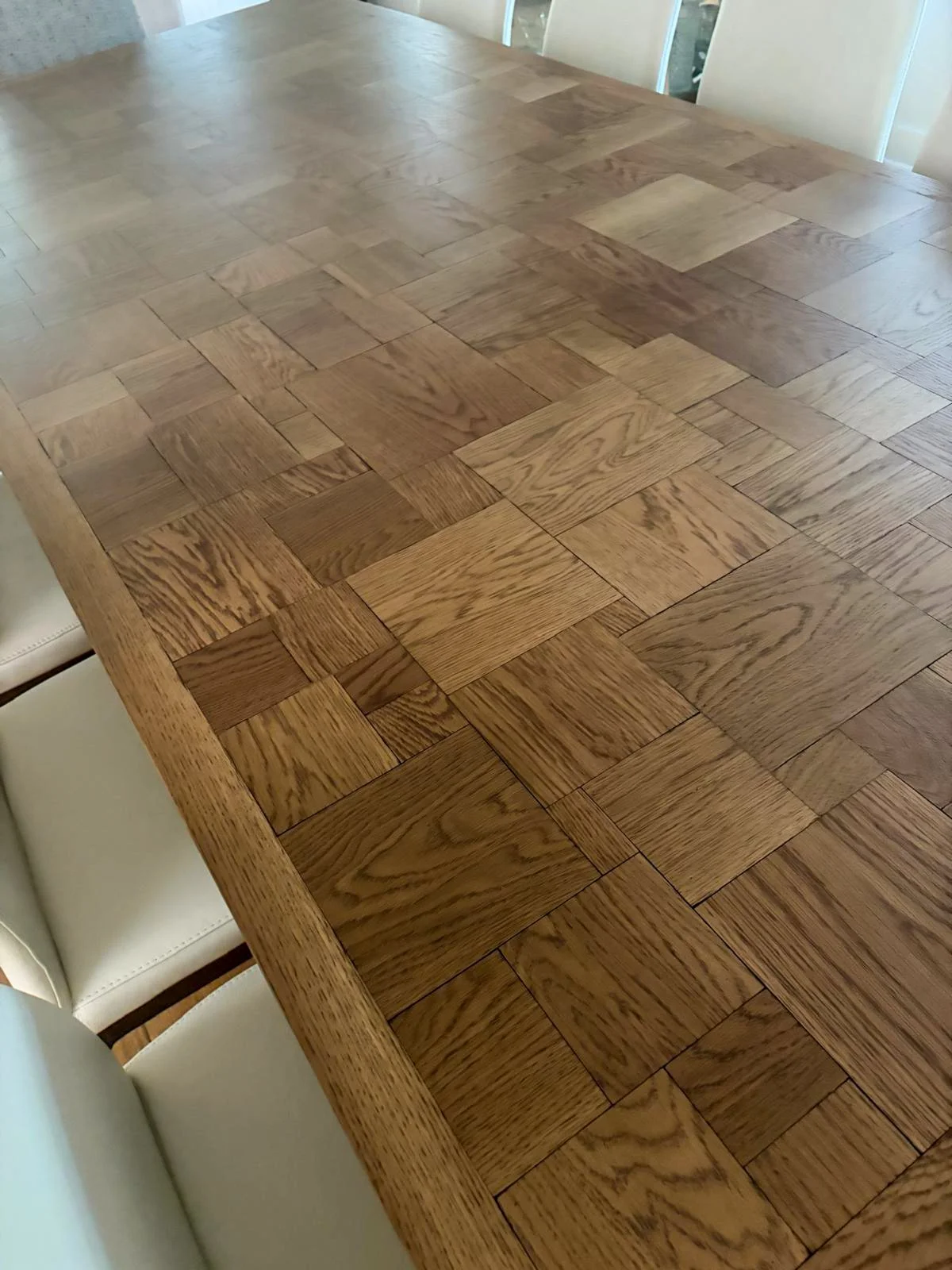 Custom white oak dining table with parquet top in light walnut finish, leather ivory side chairs, and custom reupholstered head chair in performance fabric.