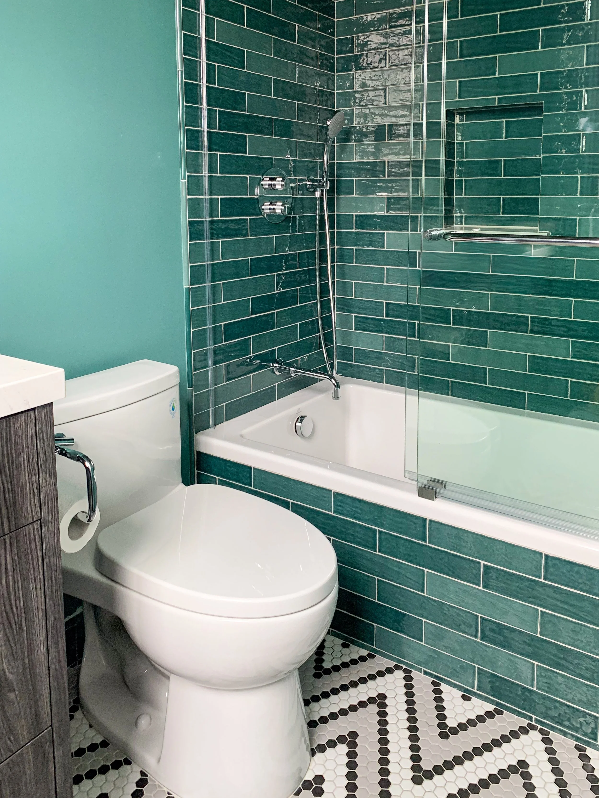 Bathroom color-drenched in teal paint and subway tile, featuring an alcove bathtub with a tiled front, a frameless shower enclosure, chrome hardware, and a black, white, and gray mosaic tile floor.
