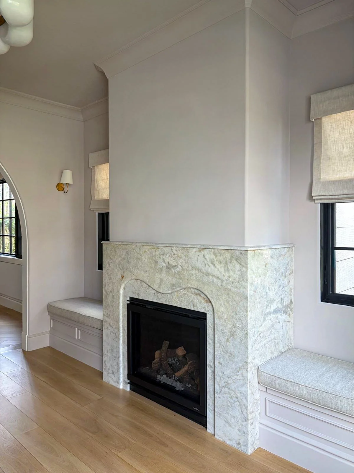Beverlywood living room featuring a marble fireplace with a black insert, flanked by built-in reading nooks with bench seating and gold sconces.