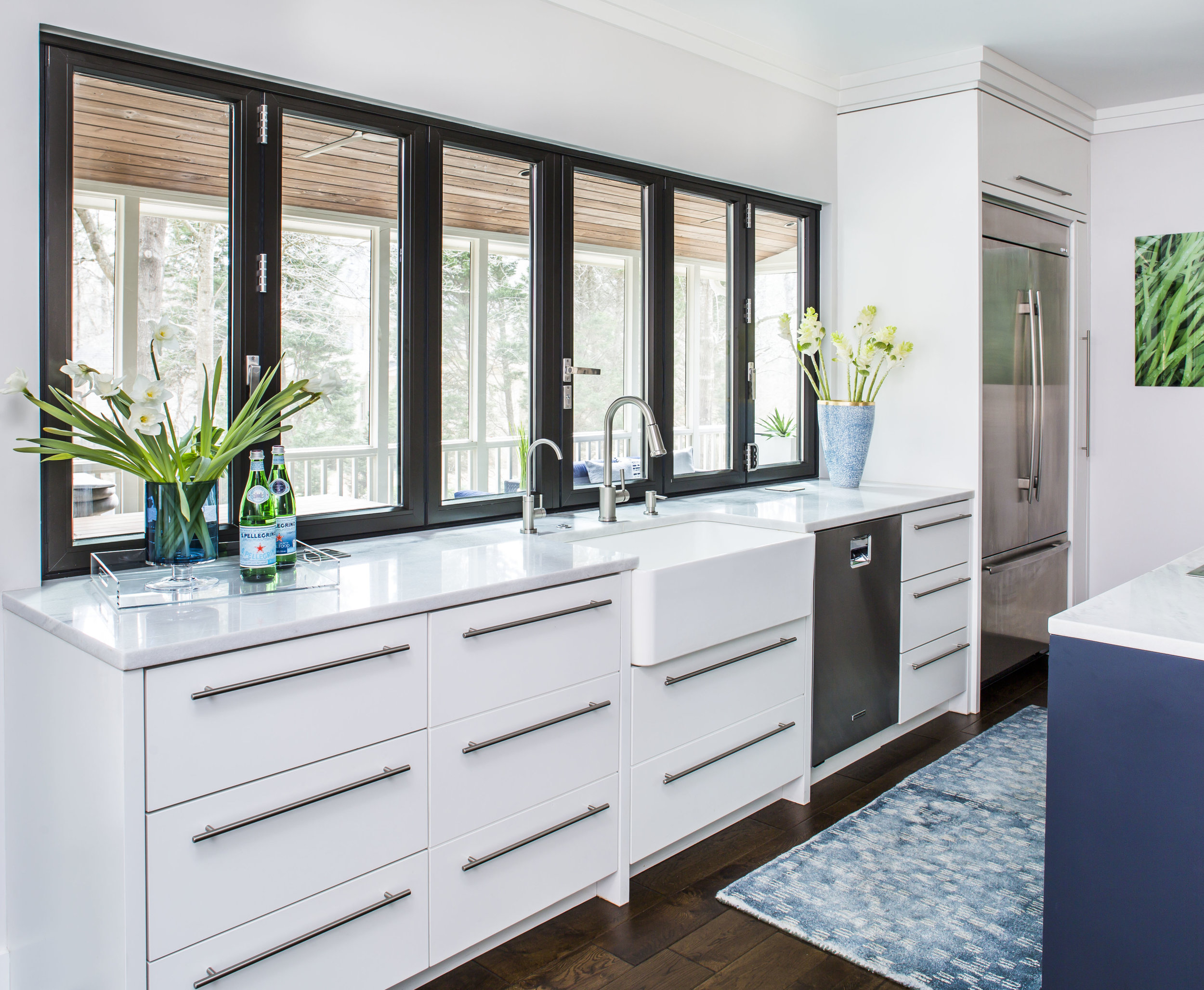 Contemporary kitchen with white cabinetry, apron sink, stainless steel appliances and accordion windows