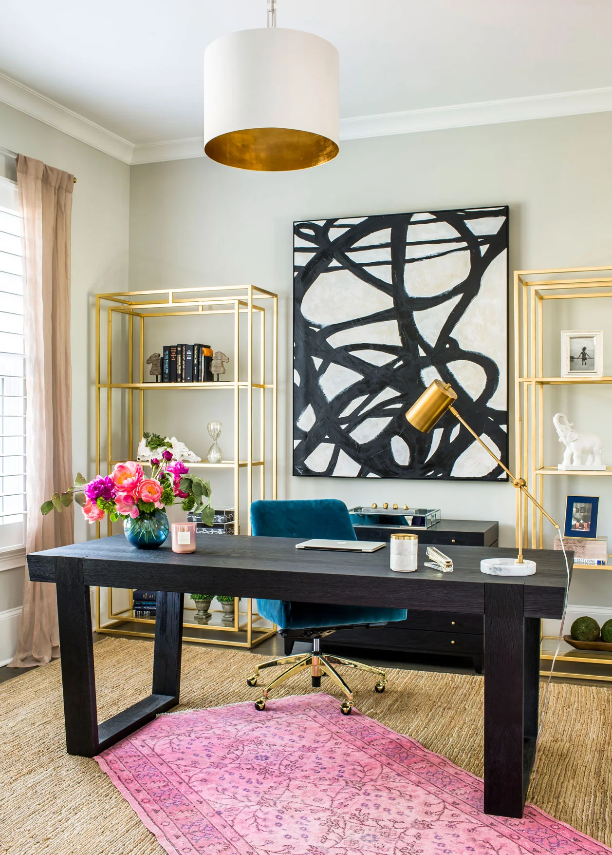 Colorful home office with freestanding desk, abstract art, pink rug and brass shelves