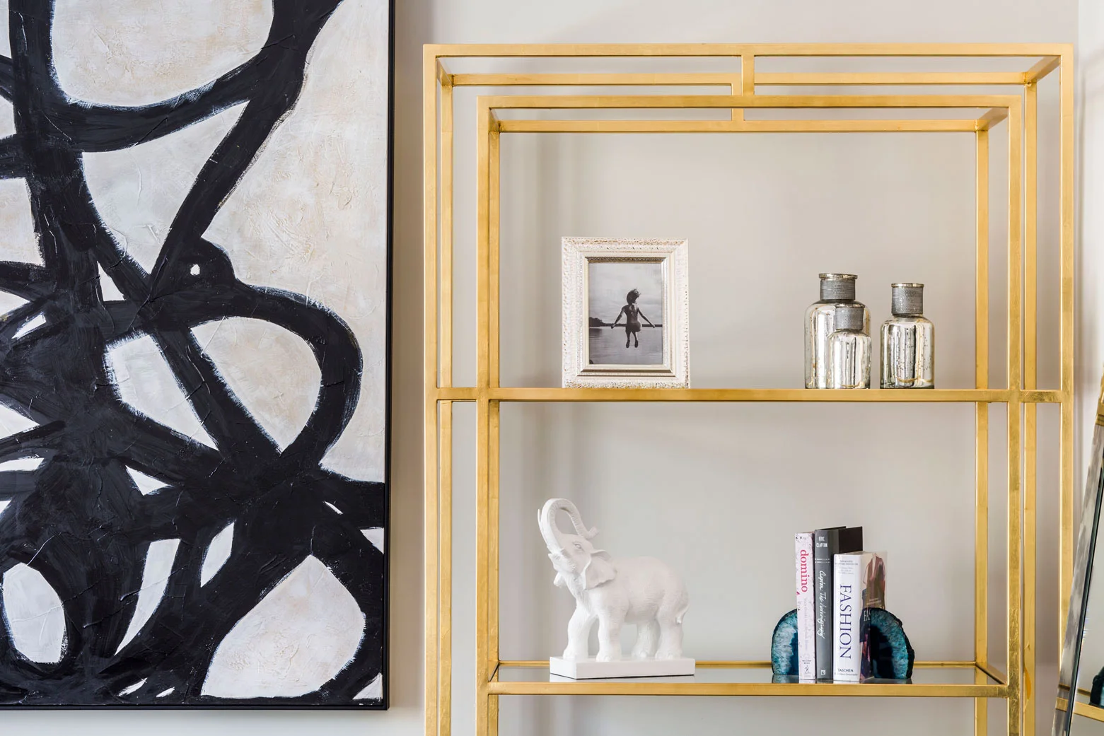 Brass shelving with books, crystal geode bookends, picture frames, and decorative glass jars