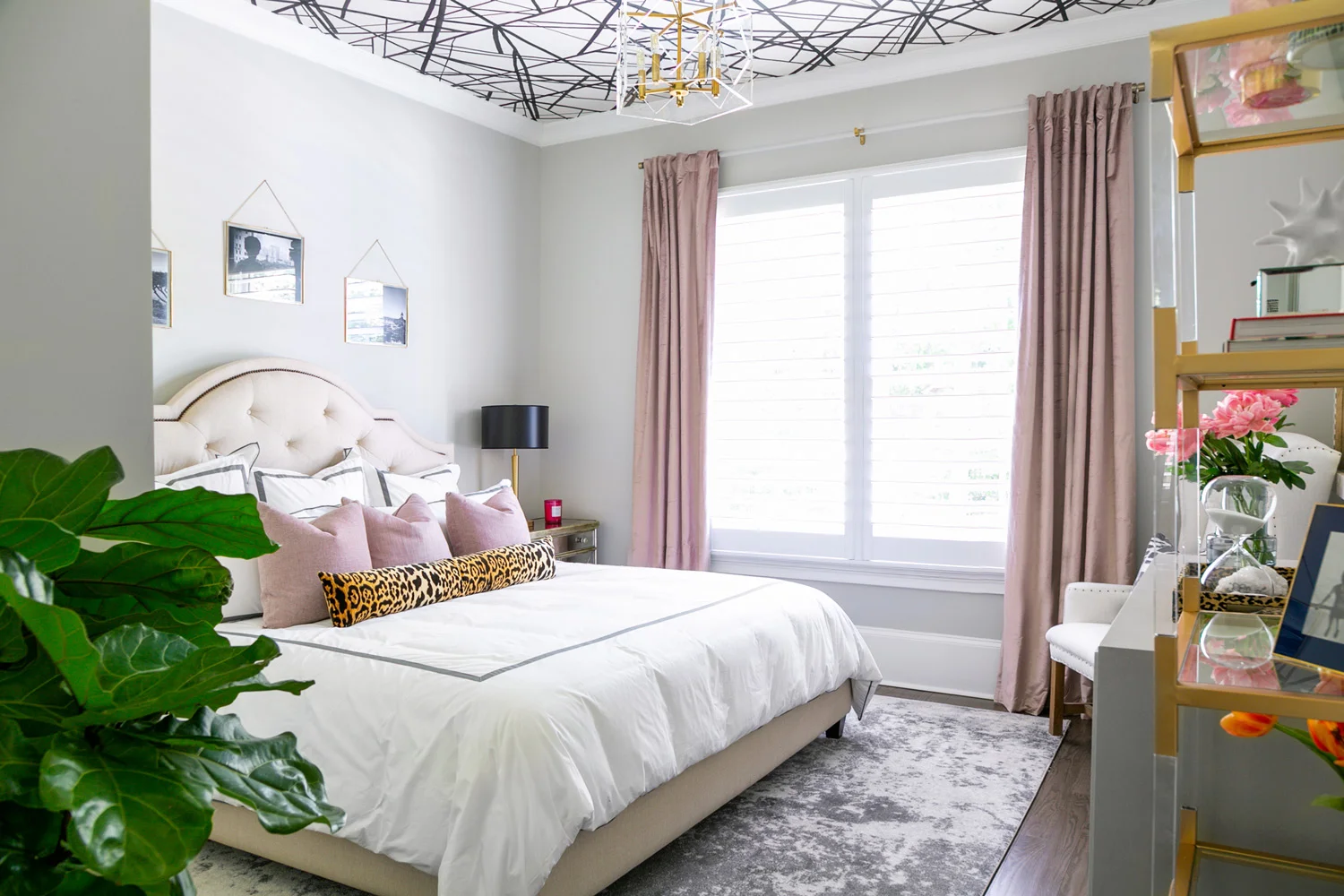 Guest bedroom with abstract wallpapered ceiling, brass lighting, and pink velvet decor