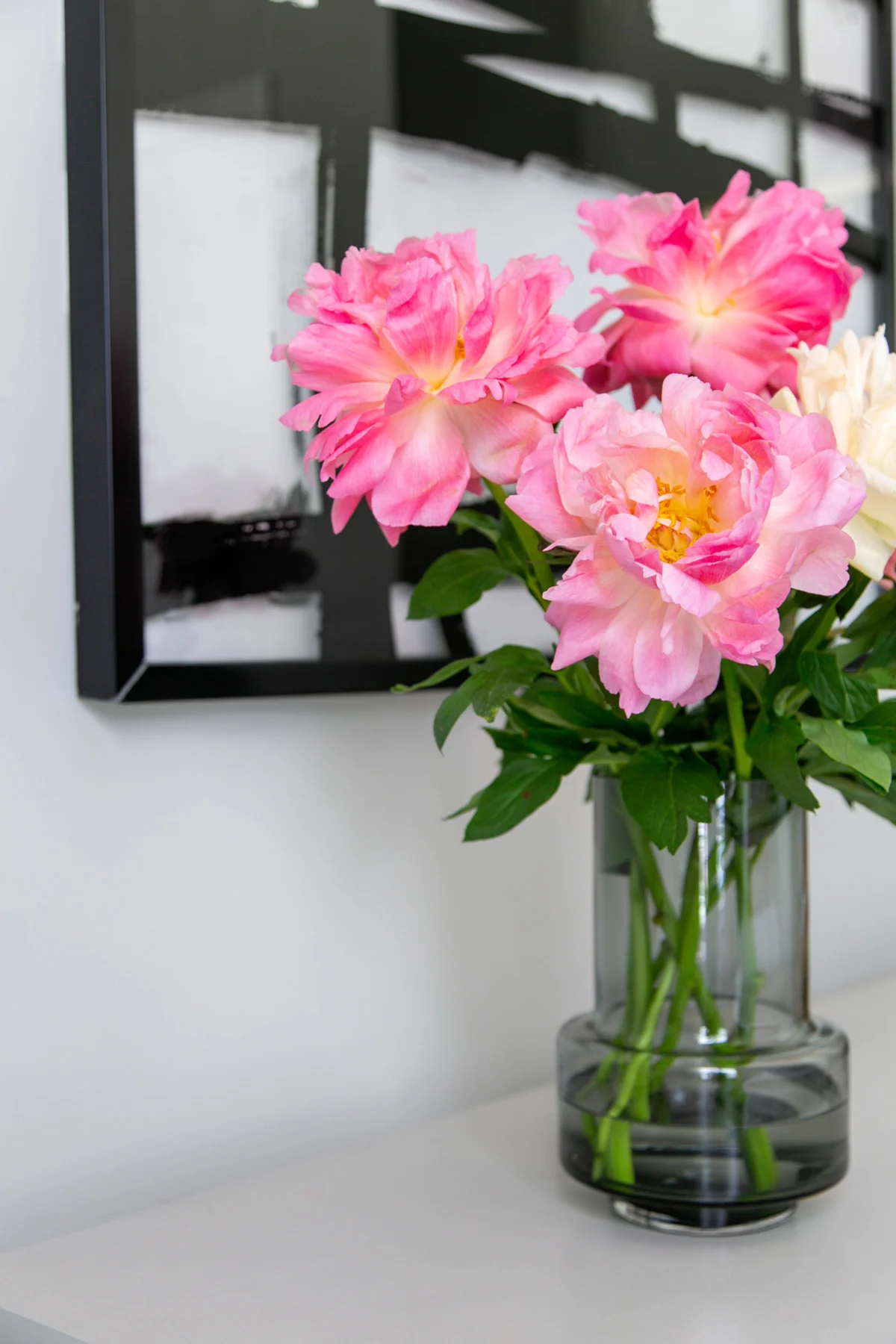 Glass vase of peonies on dresser in front of black and white abstract art