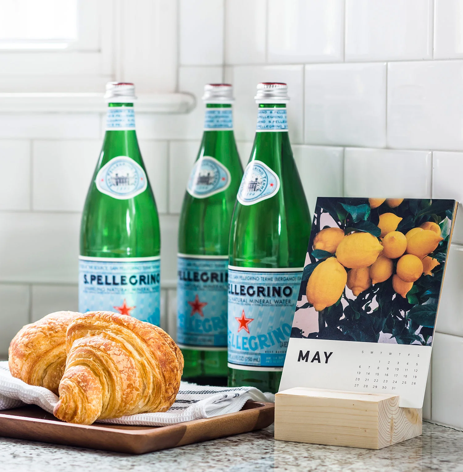 Croissant and sparkling water sitting on a kitchen counter next to calendar