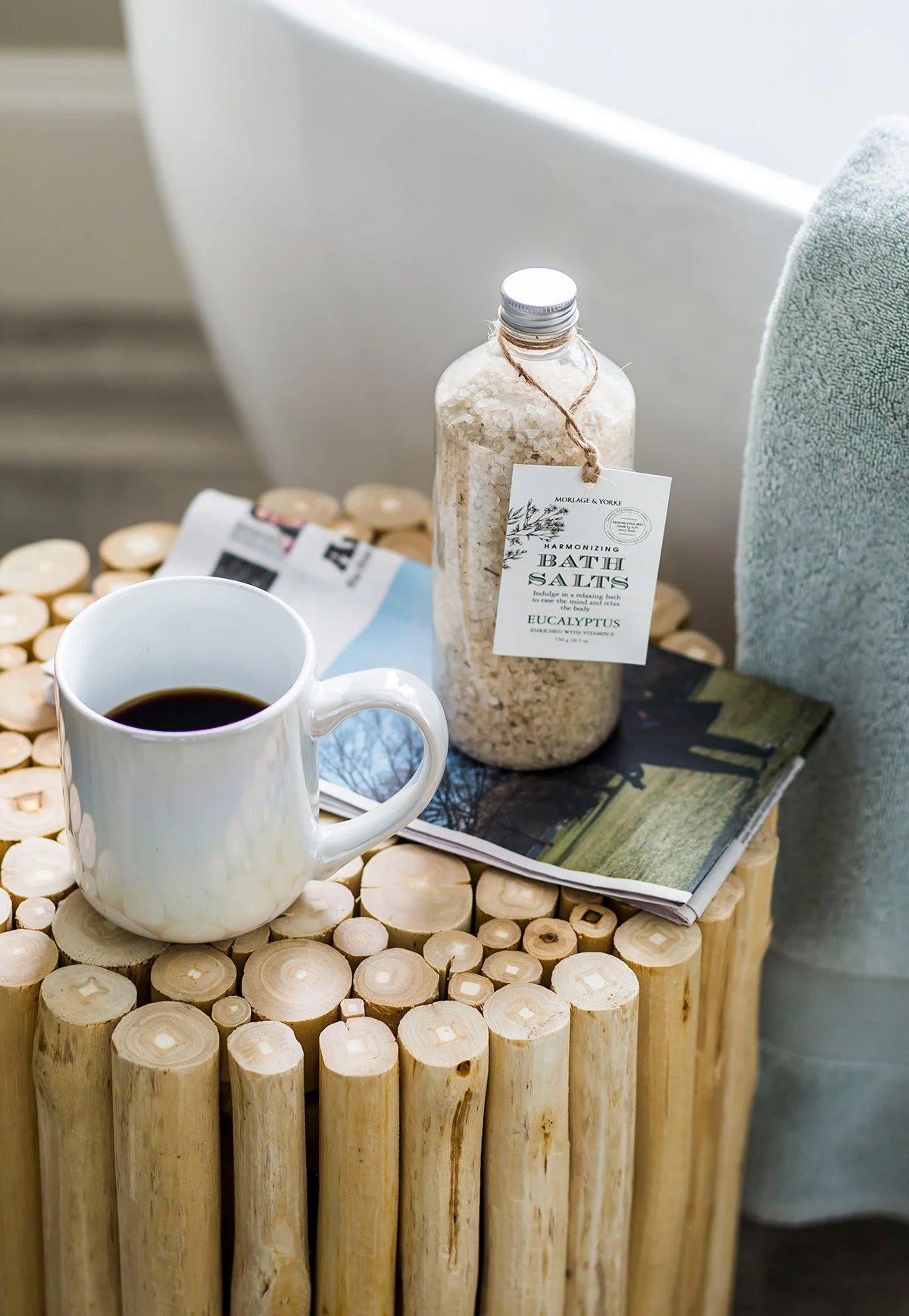 Wood stool in master bathroom with bath salts, a magazine, and a cup of coffee