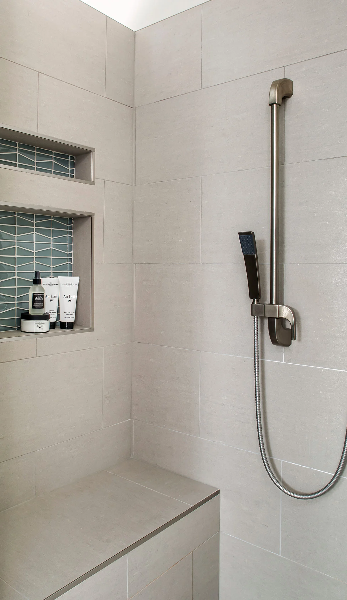 Master bathroom shower with grey tiles, bench, niche, and handheld shower head