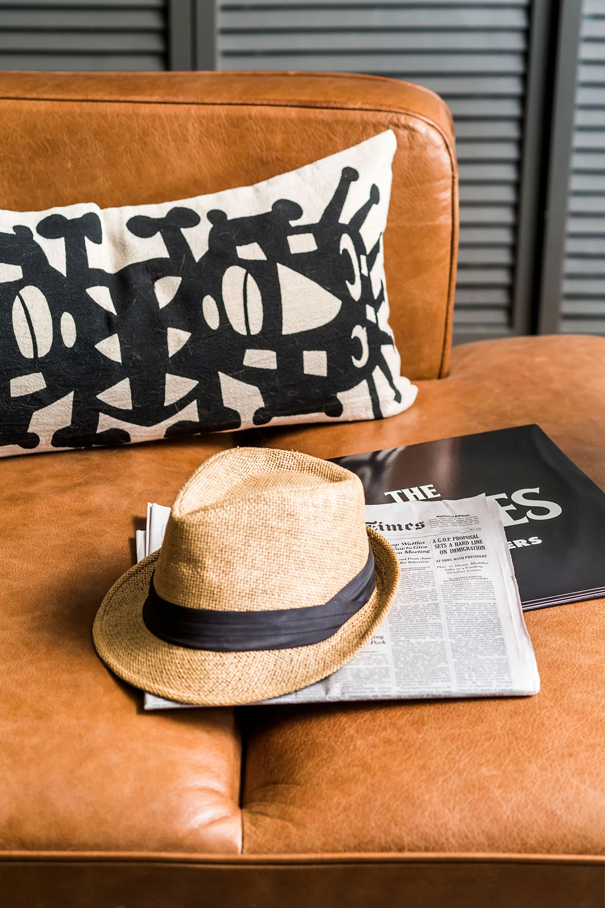Leather chaise with black and white throw pillow, newspaper, and hat