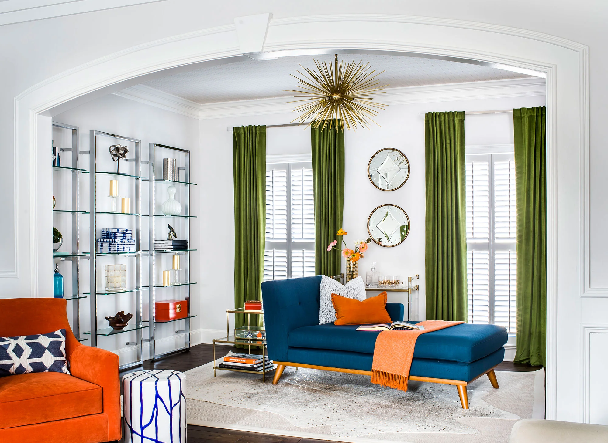 Contemporary sitting room with glass storage, green velvet curtains, and blue midcentury modern chaise