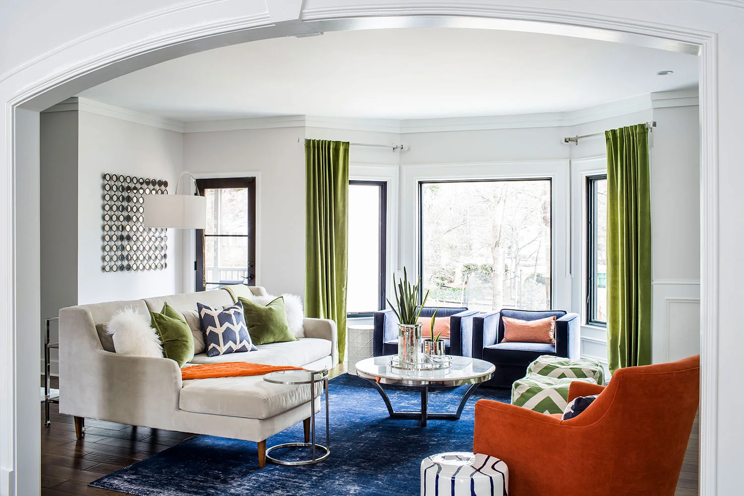 Living room with navy area rug, beige sectional and a mix of midcentury modern and contemporary styling