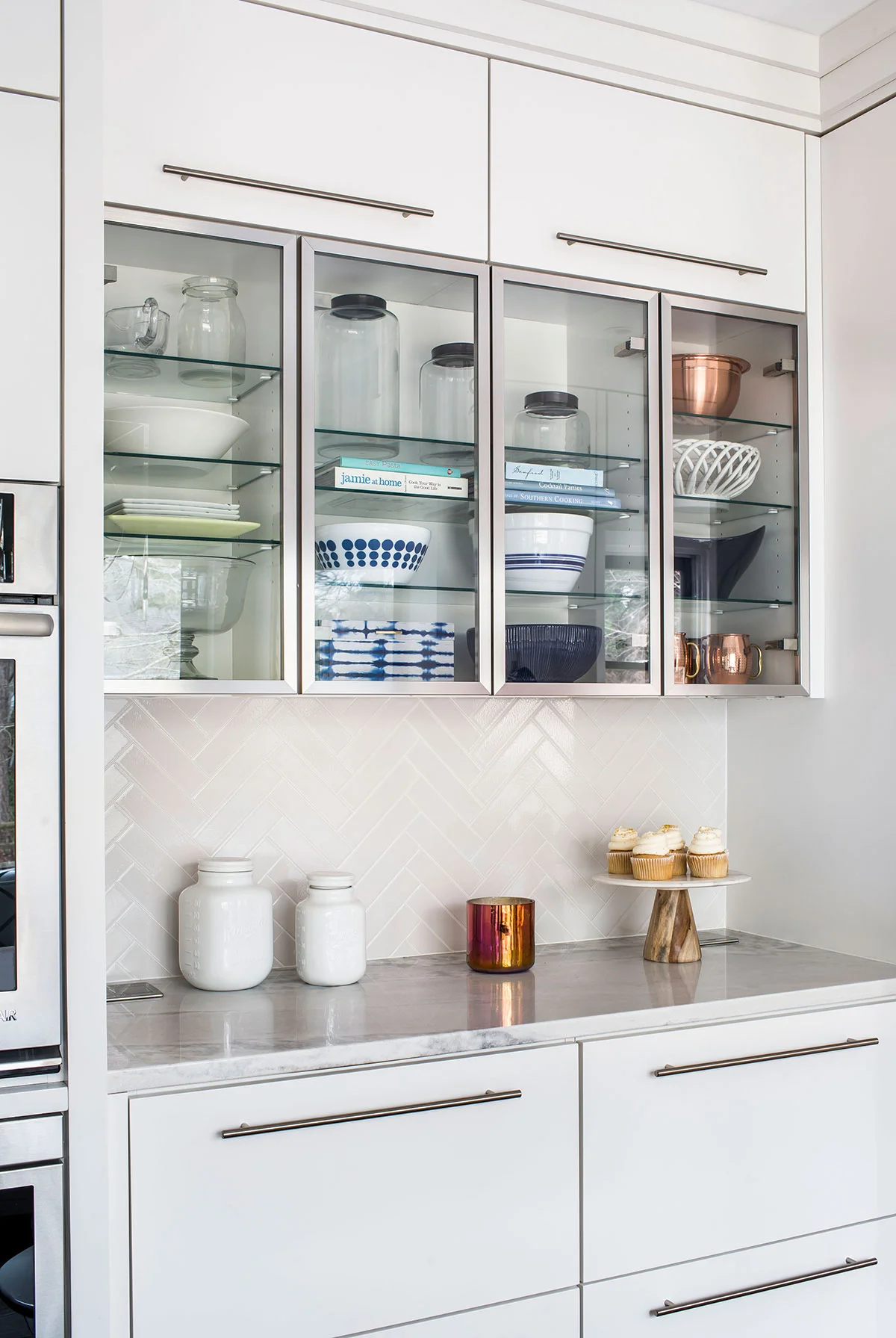 Contemporary kitchen with white backsplash, marble countertops, and glass shelving