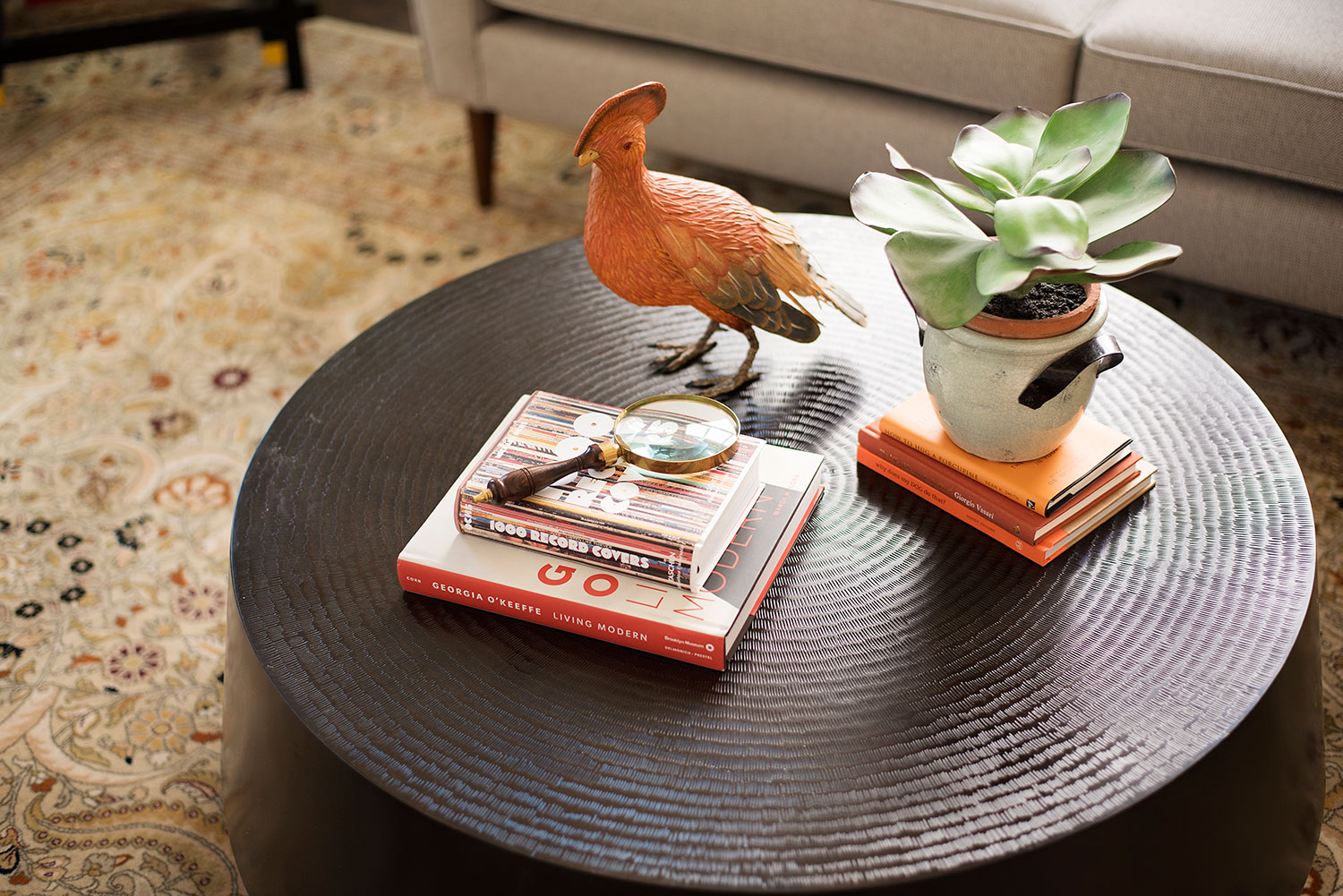 Round metal coffee table with books, potted plants and bird decor