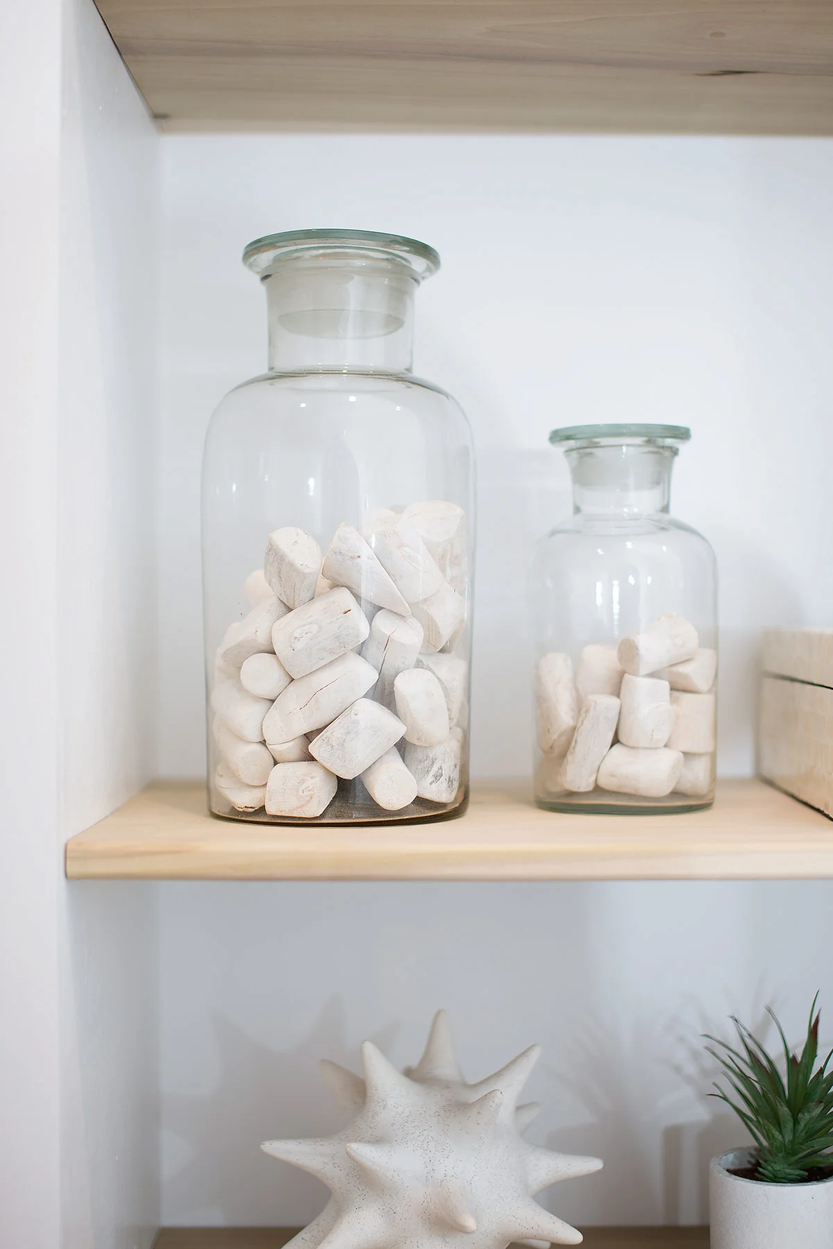 Glass bottles with coastal pebbles on built-in shelves in guest bathroom