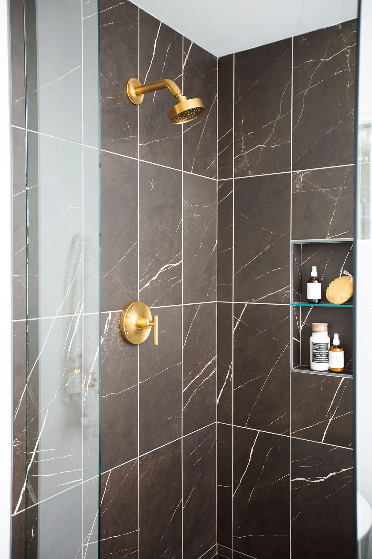 Walk-in shower with black marble tiles and brushed brass hardware in master bathroom