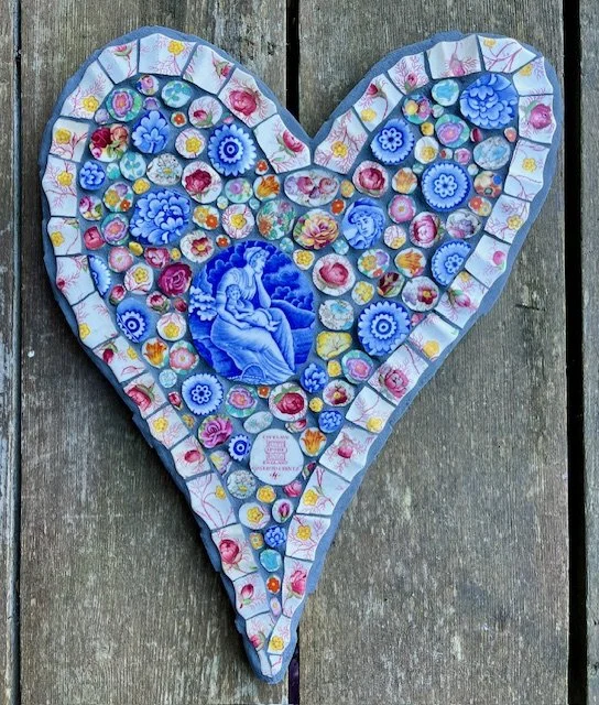 A heart shaped mosaic made with dish ware. Picture of woman holding baby in centre, flowers all around her.