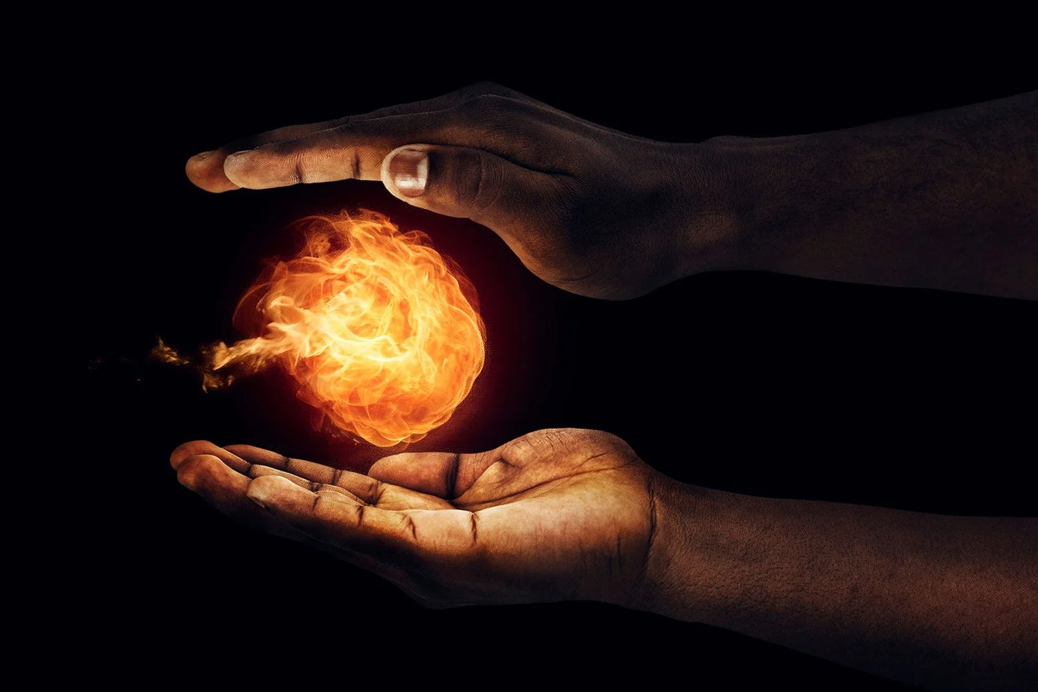 Two dark-skinned hands are positioned around a glowing orb of fire against a black background, one hand above and one below, creating a protective gesture.