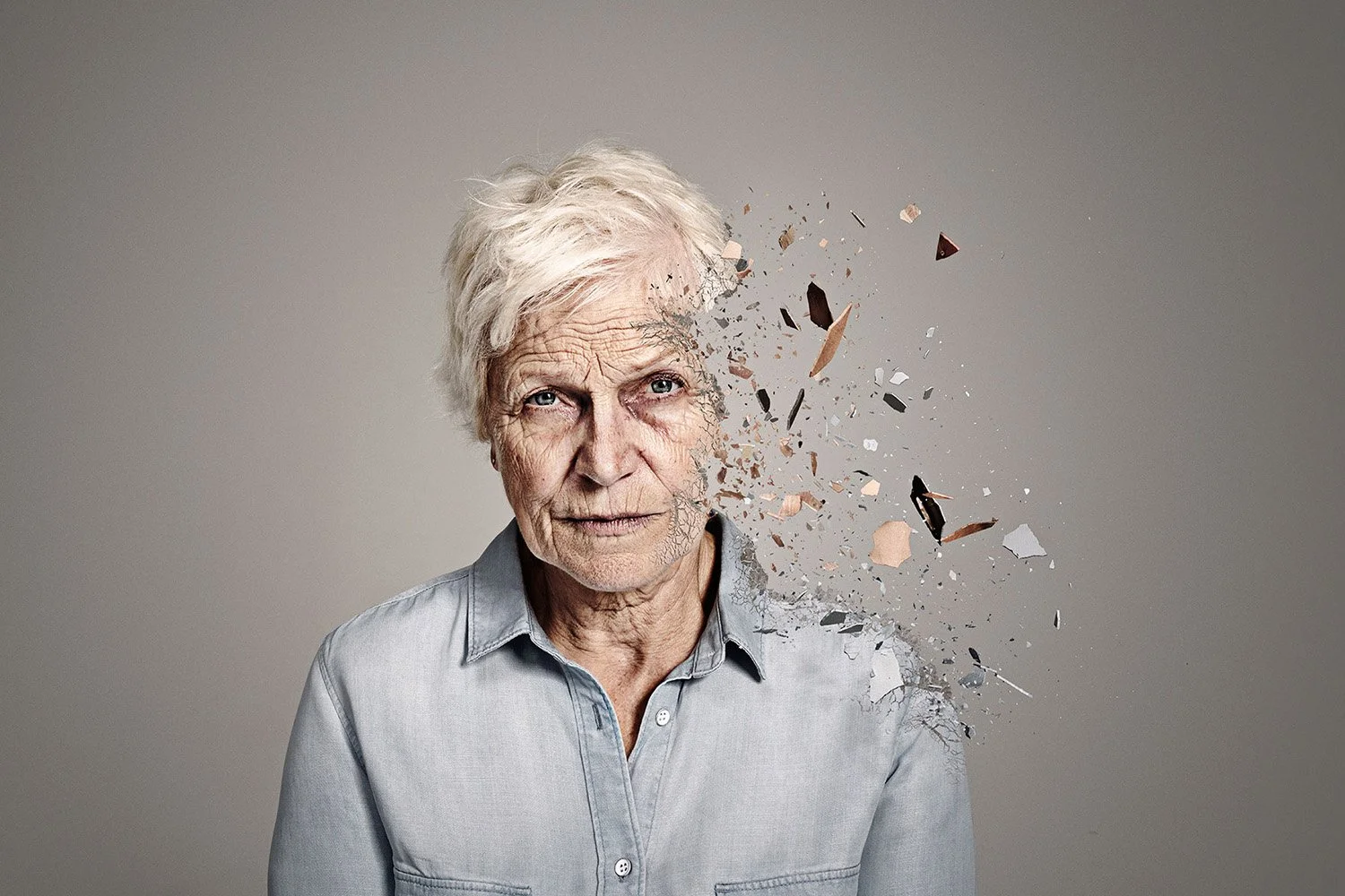 An elderly woman with white hair and a light gray shirt appears to have part of her face disintegrating into fragments, giving an artistic digital effect.