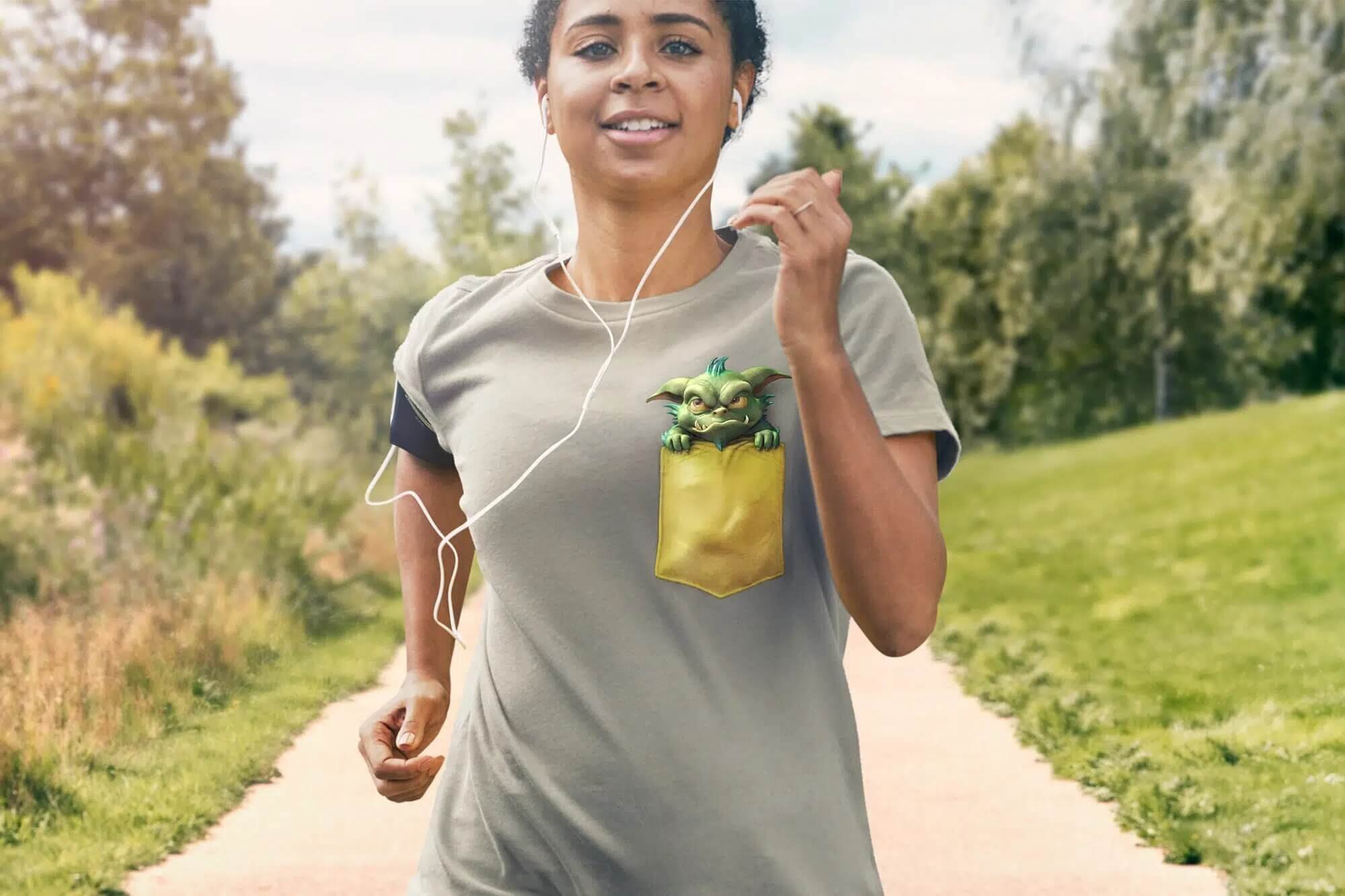 A woman jogging outdoors wearing a gray T-shirt with a cartoon character peeking out of her pocket, listening to music with earphones on a sunny day.