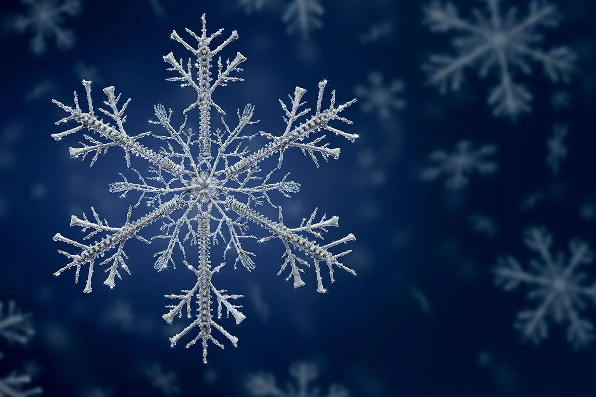 Close-up of a snowflake against a dark blue background with blurred snowflakes.