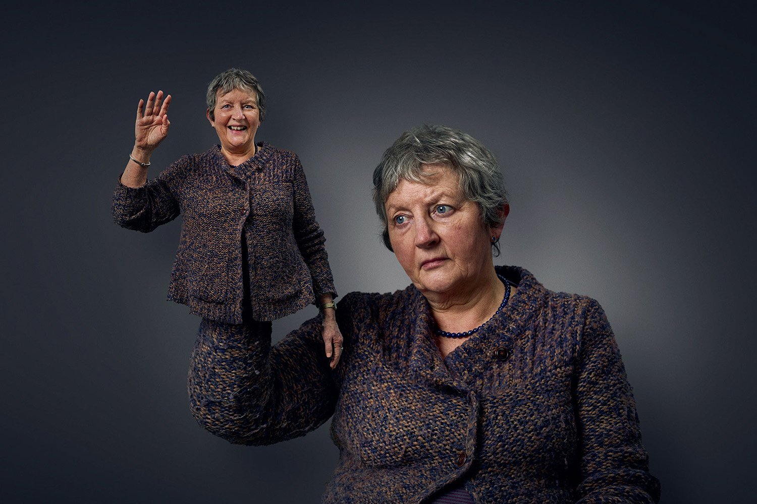 A digitally manipulated image features two views of a woman with short gray hair, wearing a matching mixed-color blazer and skirt. One view shows her smiling and raising her right hand in a wave, while the other shows her with a serious expression, l
