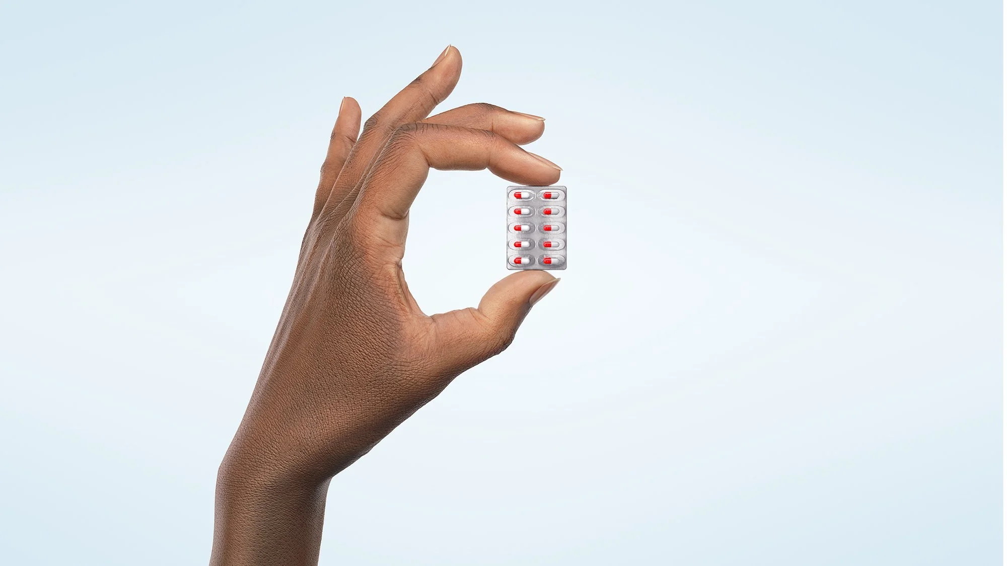 Hand holding a blister pack of pills with a light blue background.
