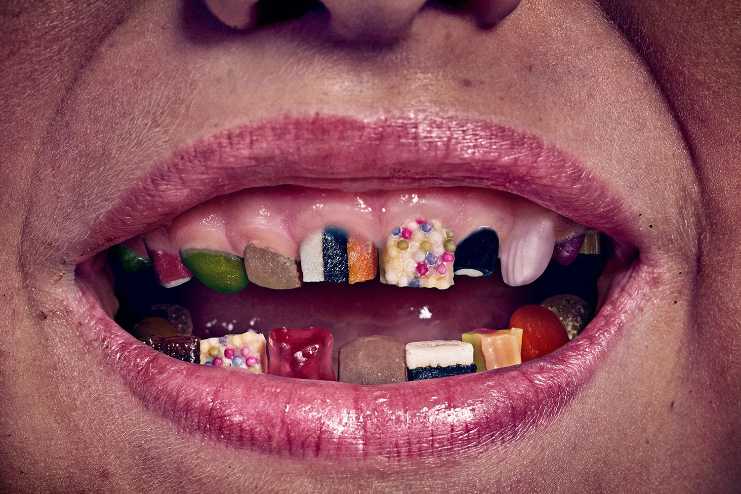Close-up of a person's open mouth filled with a variety of colorful candies and gummy candies.